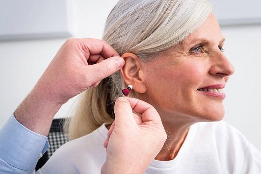 Eine Frau bekommt ein modernes Hörgerät vom Hörakustiker ins Ohr eingesetzt.